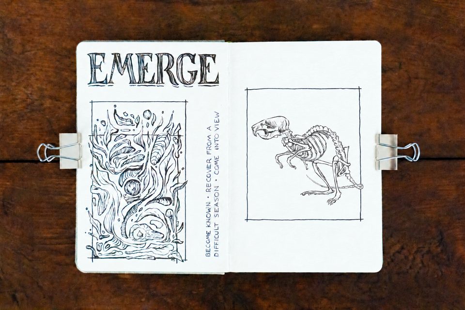 Open sketchbook on a wooden tabletop, with EMERGE lettering and a framed tree drawing on the left page and a rat skeleton inside a hand-drawn rectangular border on the right.